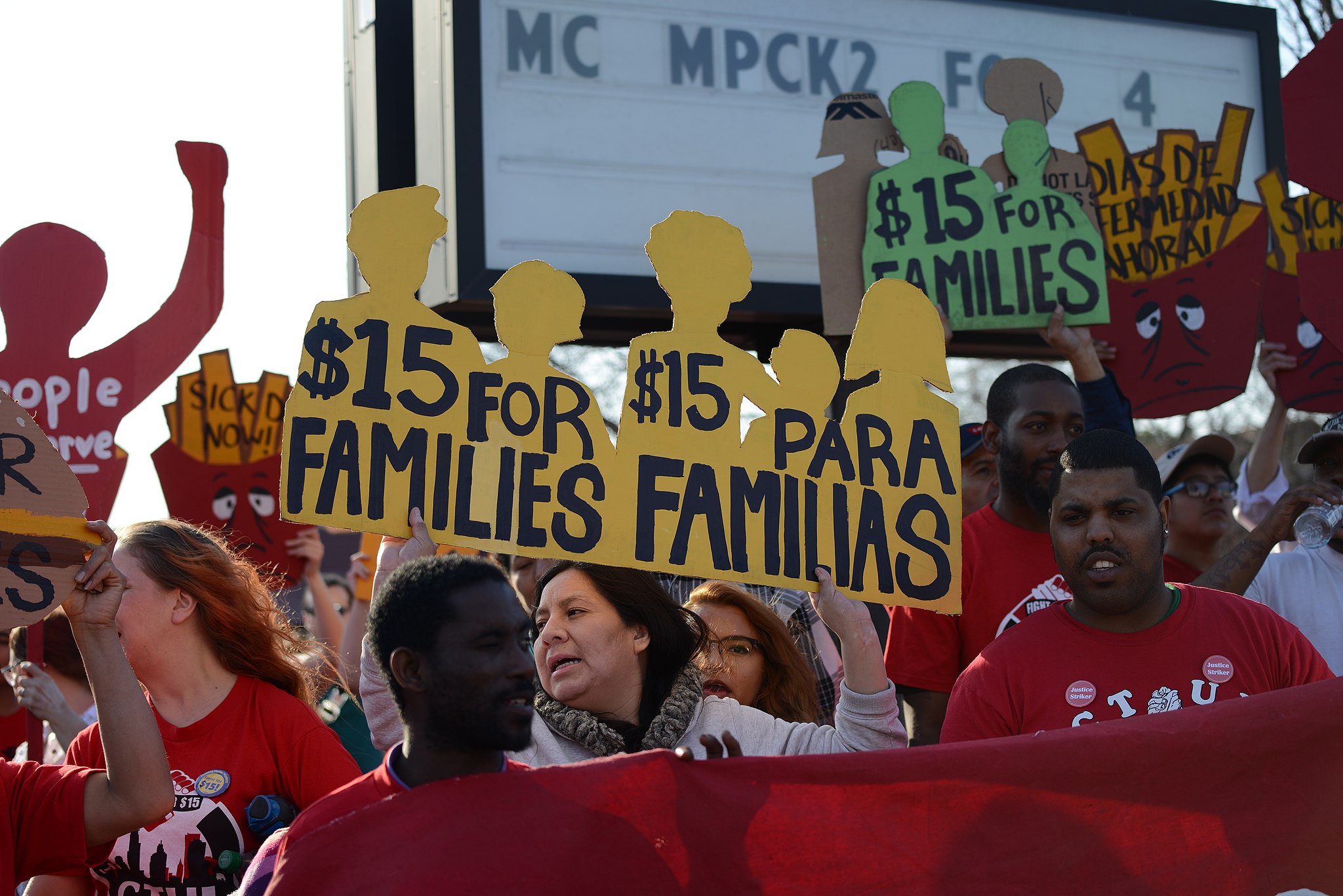 Striking workers wearing red shirts and carrying signs that read "$15 for families/$15 para familias"