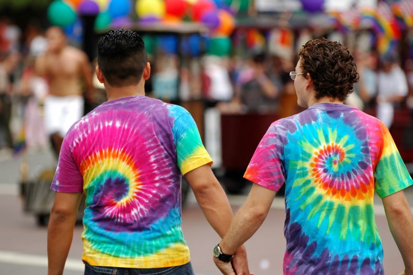 Two men hold hands, wearching rainblow tie-dyed shirts