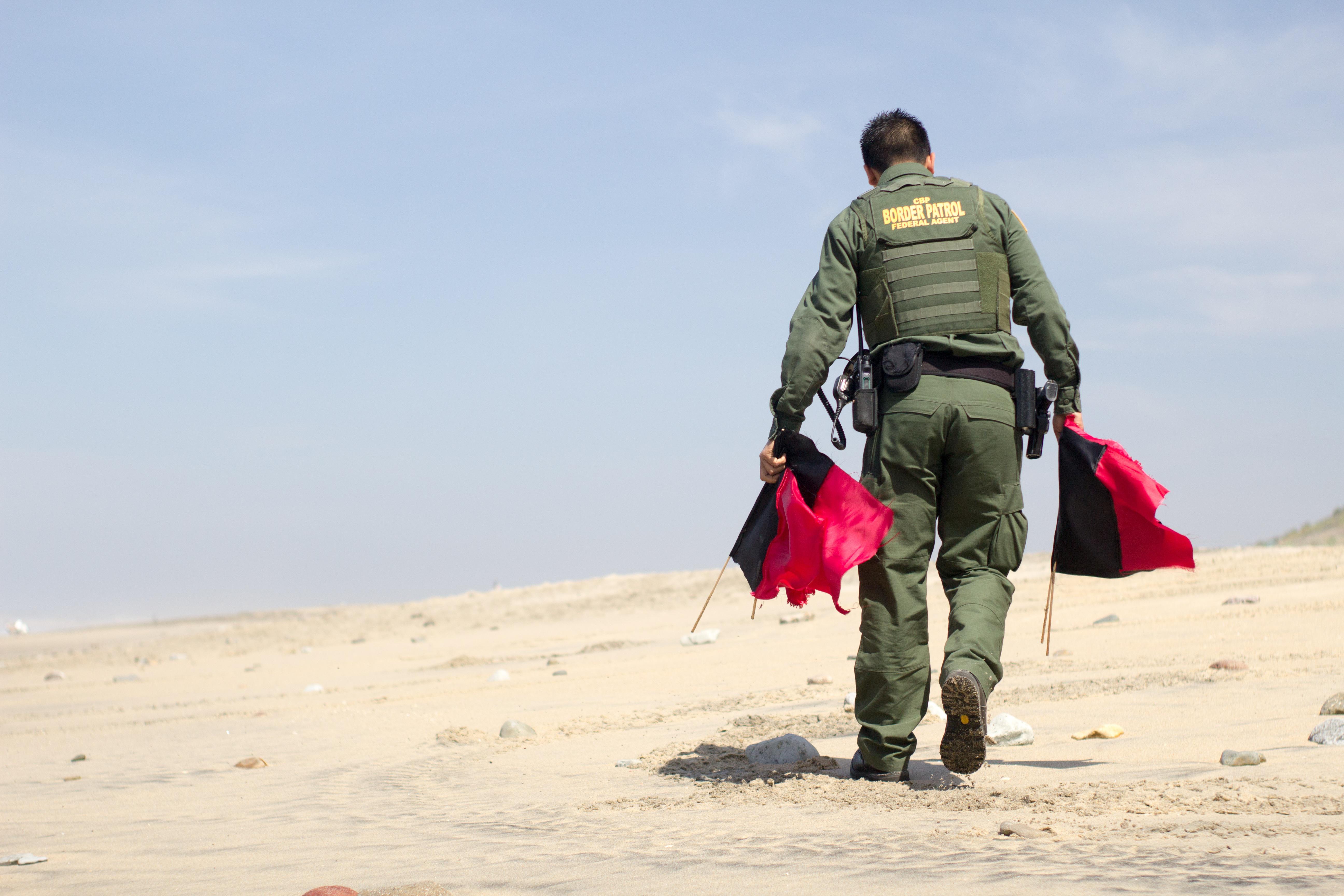 CBP Border Patrol agent carries red and black flags while patrolling the desert.