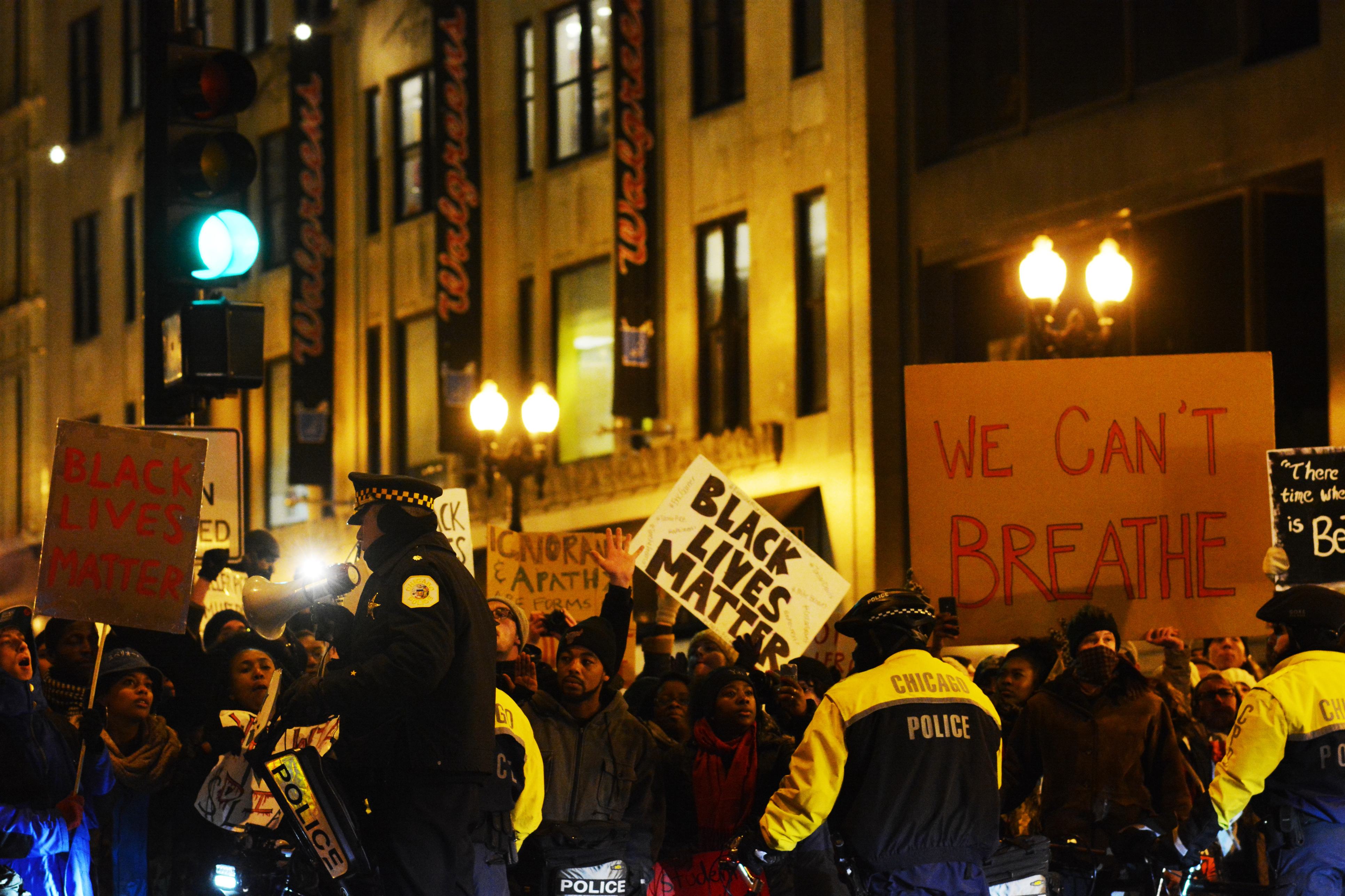 A crowd of protestors with signs gather in the streets to protest against police brutality against African Americans as the Chicago Police standby.