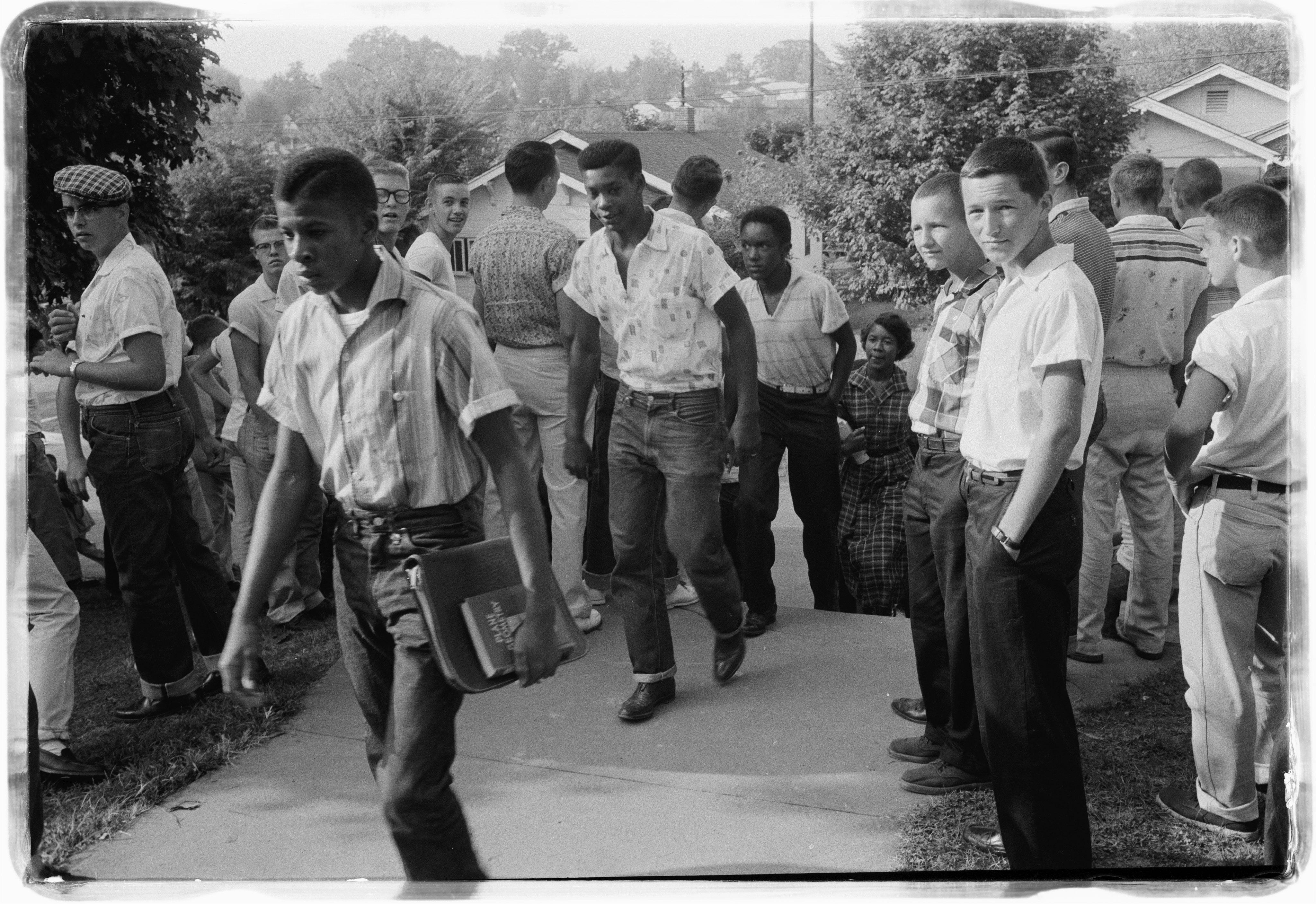 Historical B&W photo of African American students walking through a crowd of white students, with police on standby