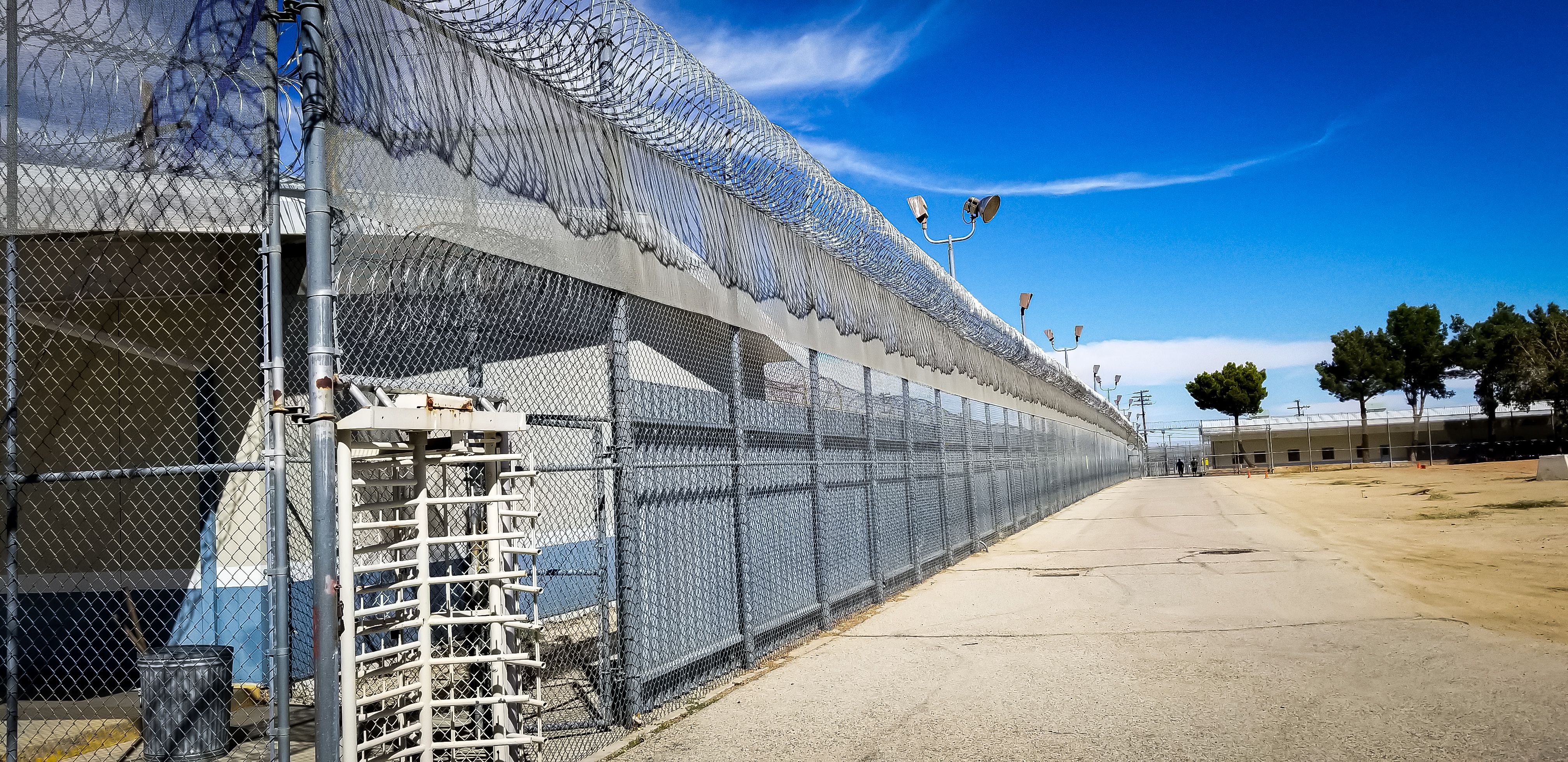 Sunlit prison fences with security wire, and turnstile of Mira Loma Detention Center in Lancaster California.