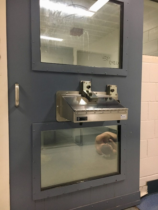 Man in Psychiatric Stabilization Unit, naked, sleeping on floor, using a roll of toilet paper between his head and the floor.